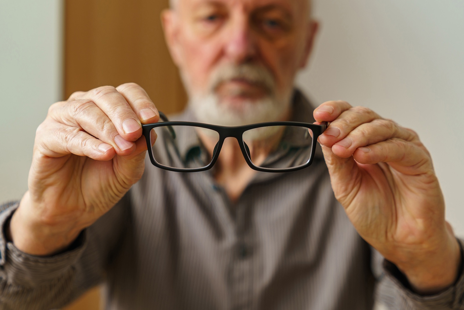 Elderly man holding glasses in front of him. Close up.